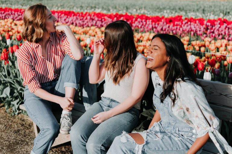 a group of women sitting on a bench in a field of red flowers